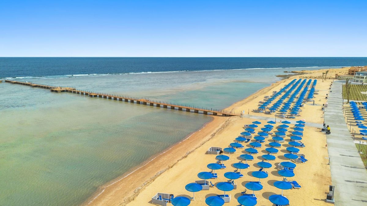 Albatros Makadi Resort beach with rows of blue umbrellas and shallow water.