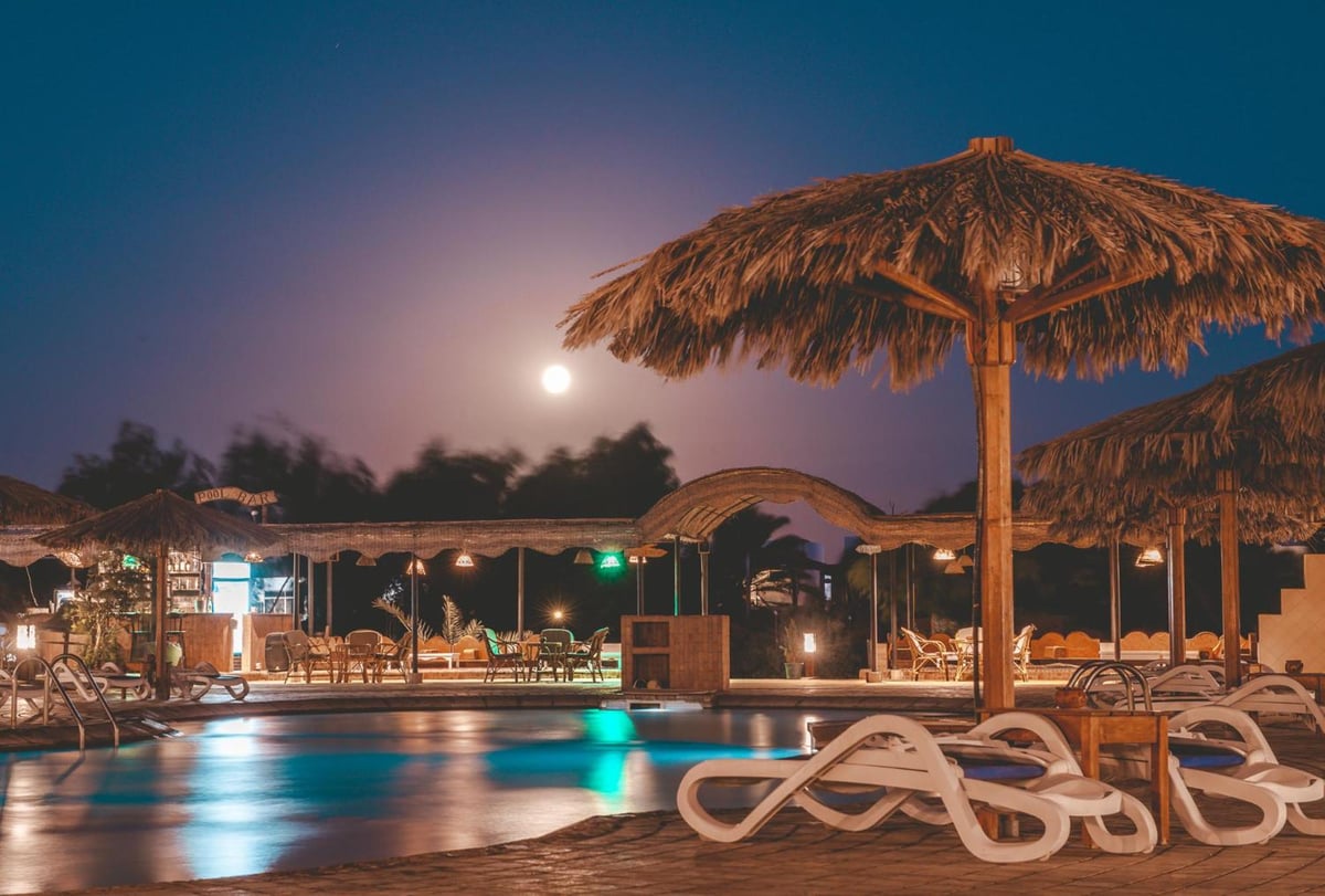 Sheikh Ali Dahab Resort pool deck with a thatched parasol and illuminated pool.