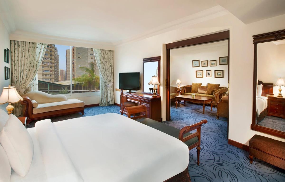 Hilton Alexandria Green Plaza bedroom suite with a large bed and adjoining sitting area.