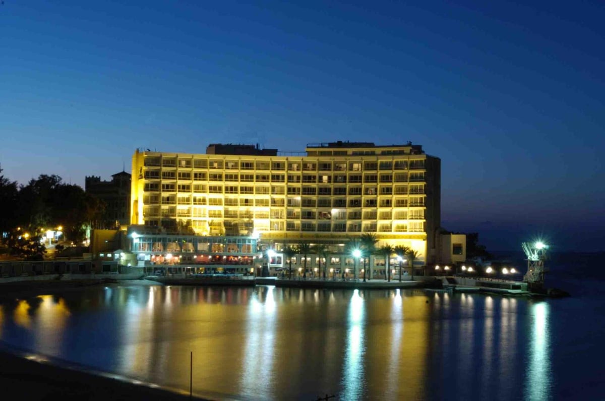Palestine Montaza Alexandria hotel with an illuminated facade and reflections on the water.
