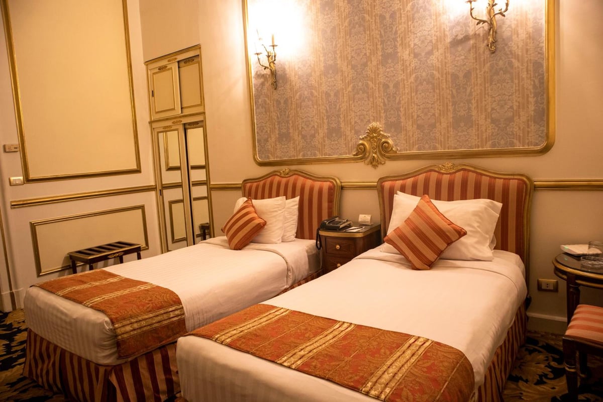 Le Metropole Hotel Alexandria twin bedroom with two beds and an ornate wall panel.
