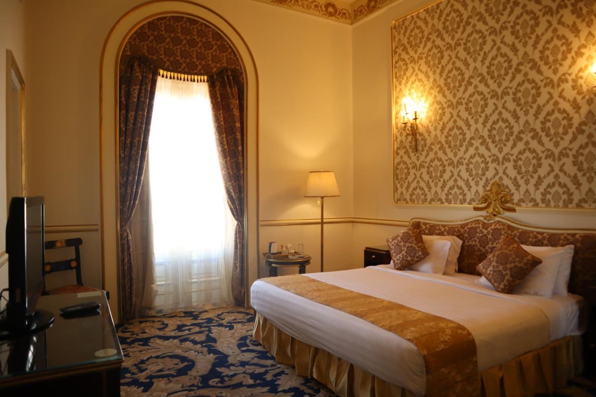 Le Metropole Hotel Alexandria bedroom with a large bed and an arched window.