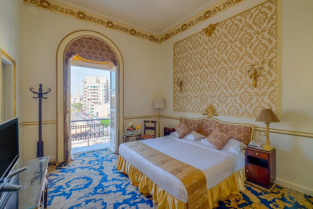 Le Metropole Hotel Alexandria bedroom with a large bed and gold-patterned walls.