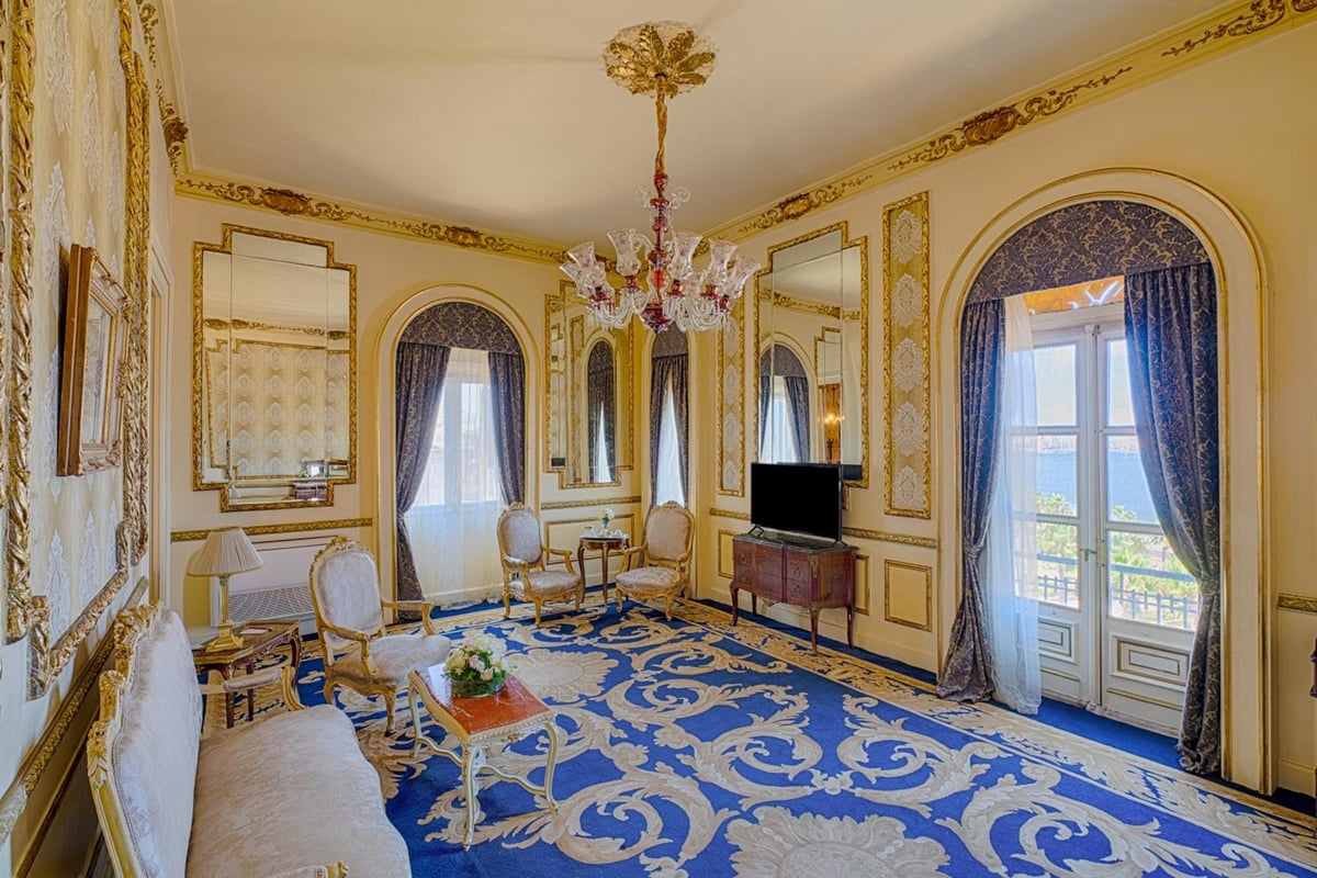 Le Metropole Hotel Alexandria sitting room with gold-trimmed walls and a blue patterned carpet.