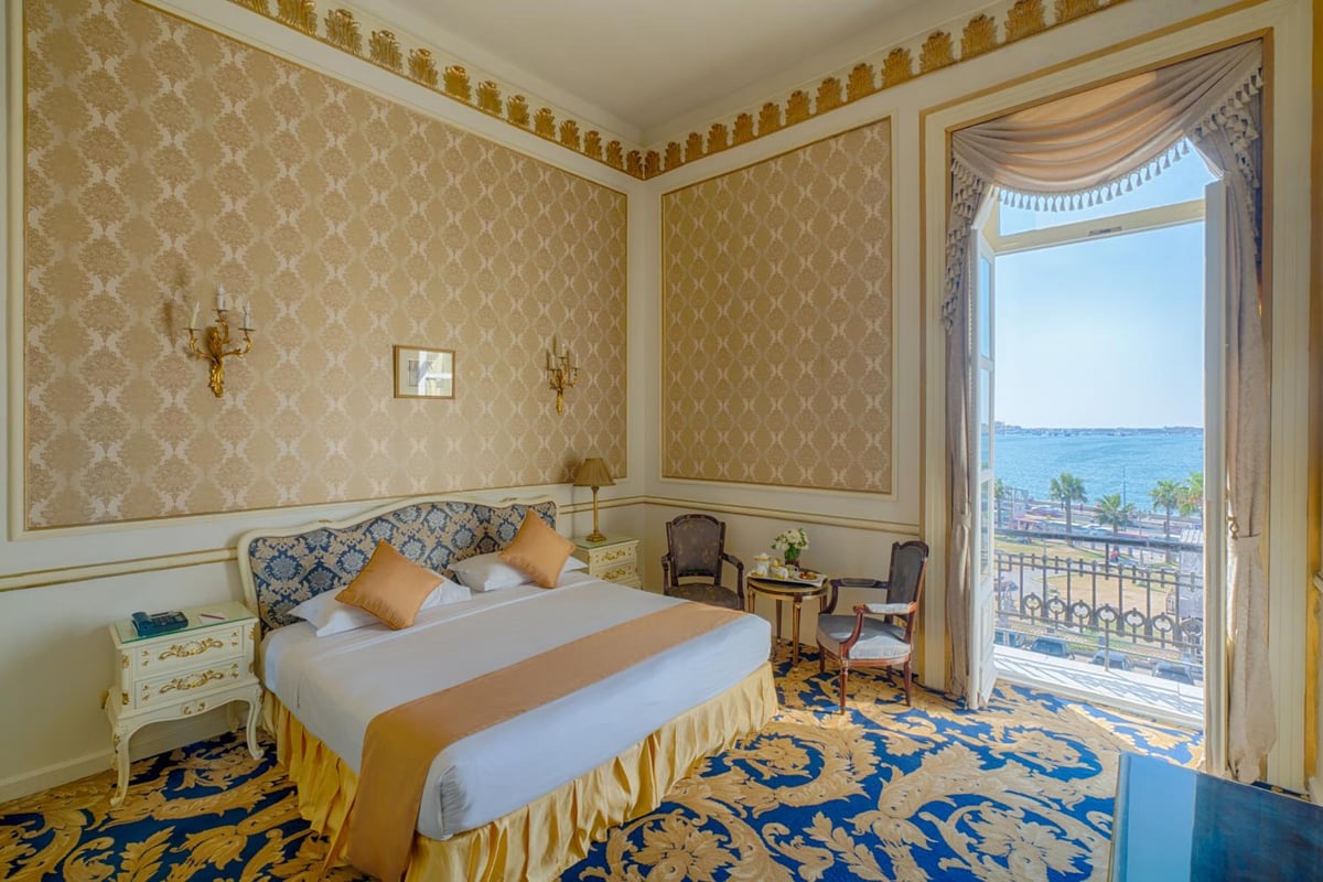 Le Metropole Hotel Alexandria guest room with a large bed and balcony overlooking the sea.