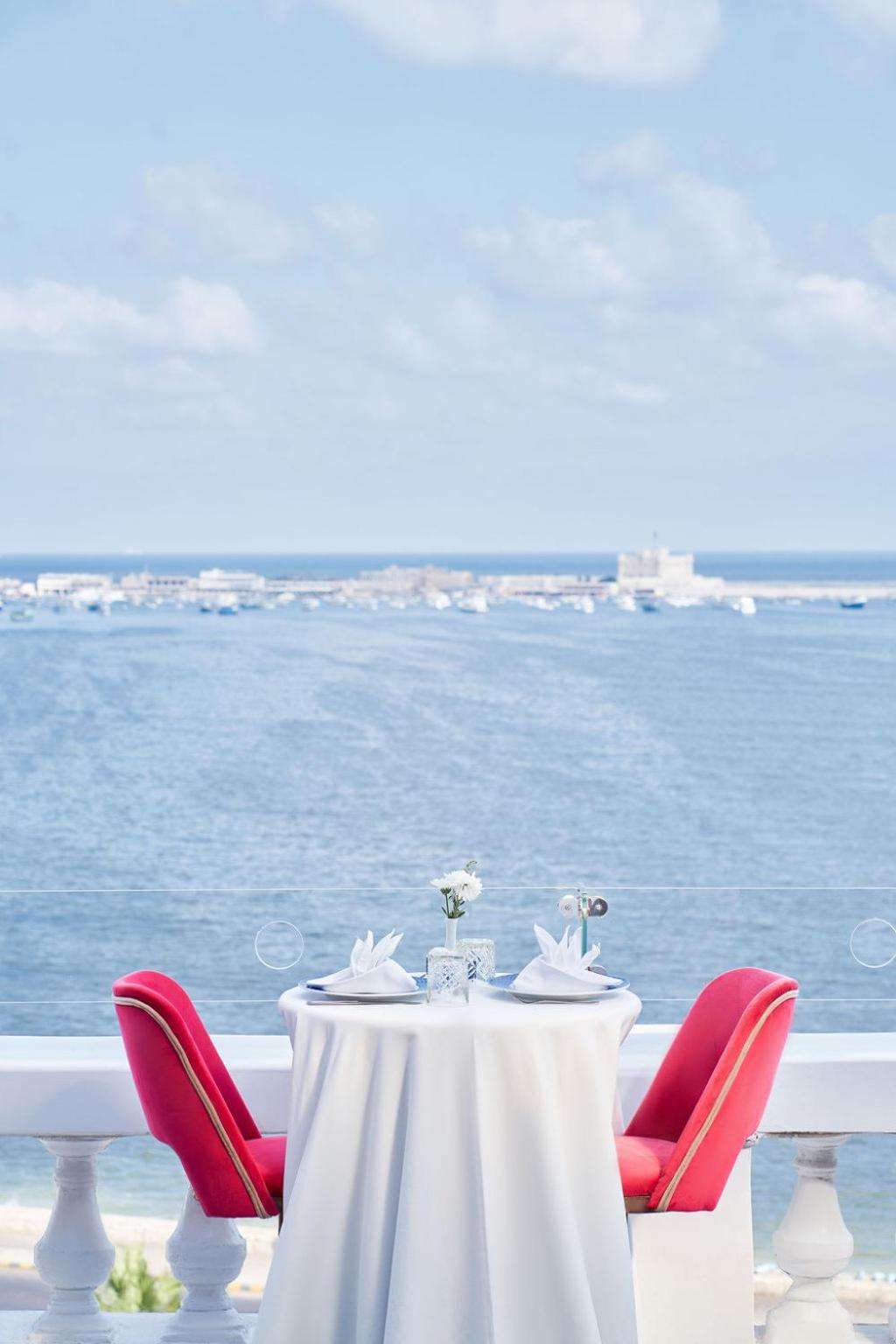 Le Metropole Hotel Alexandria terrace with a sea view and red chairs.