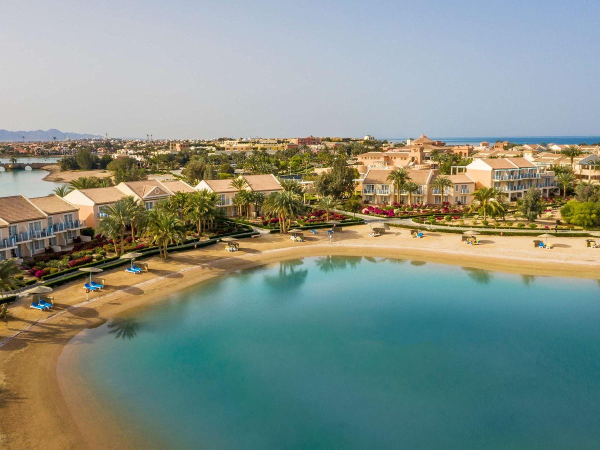 Movenpick Resort & Spa El Gouna lagoon beach with a curved sandy shore and resort buildings.