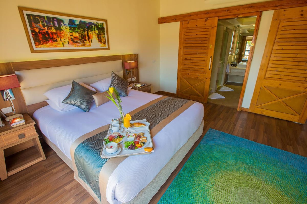 Pickalbatros Aqua Blu Sharm El Sheikh bedroom with a large bed and wooden sliding doors.