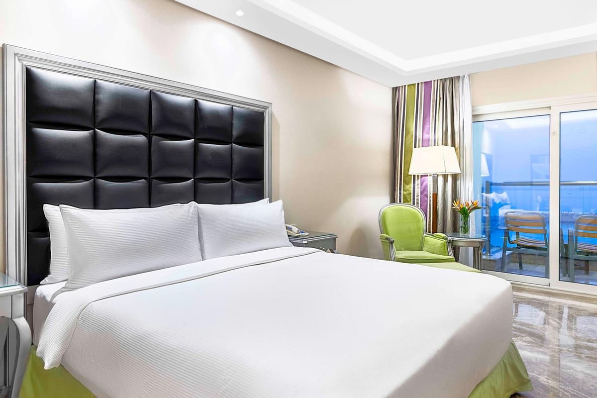 Hilton Alexandria Corniche bedroom with white bedding and sliding glass doors.