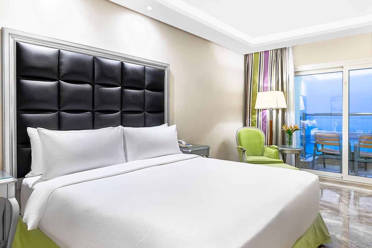 Hilton Alexandria Corniche guest room with a large bed and glass balcony doors.