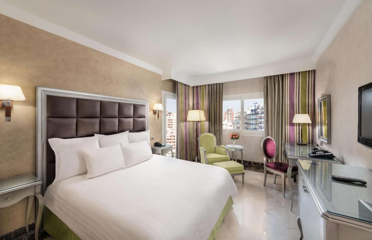 Hilton Alexandria Corniche bedroom with a large bed and striped curtains.