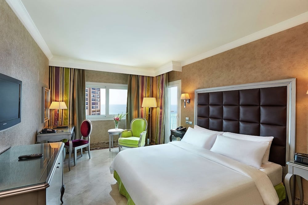 Hilton Alexandria Corniche guest room with a white bed and padded headboard.