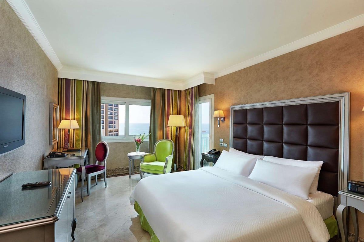 Hilton Alexandria Corniche bedroom with a white bed and padded headboard.