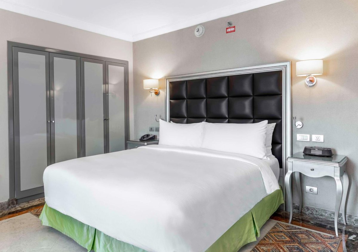 Hilton Alexandria Corniche bedroom with a tufted headboard and paneled wardrobe.
