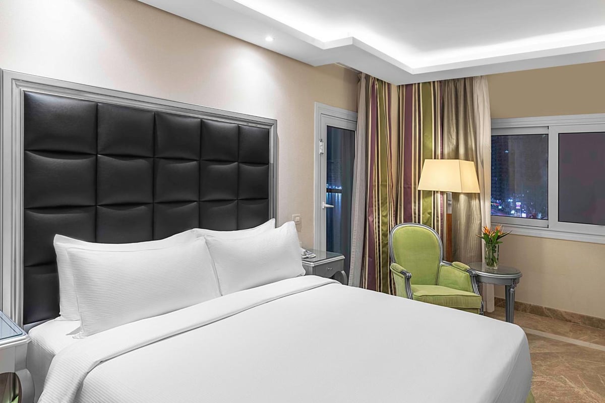 Hilton Alexandria Corniche bedroom with a black padded headboard and a green armchair.