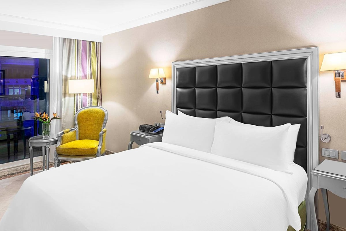 Hilton Alexandria Corniche bedroom with a white bed and black padded headboard.