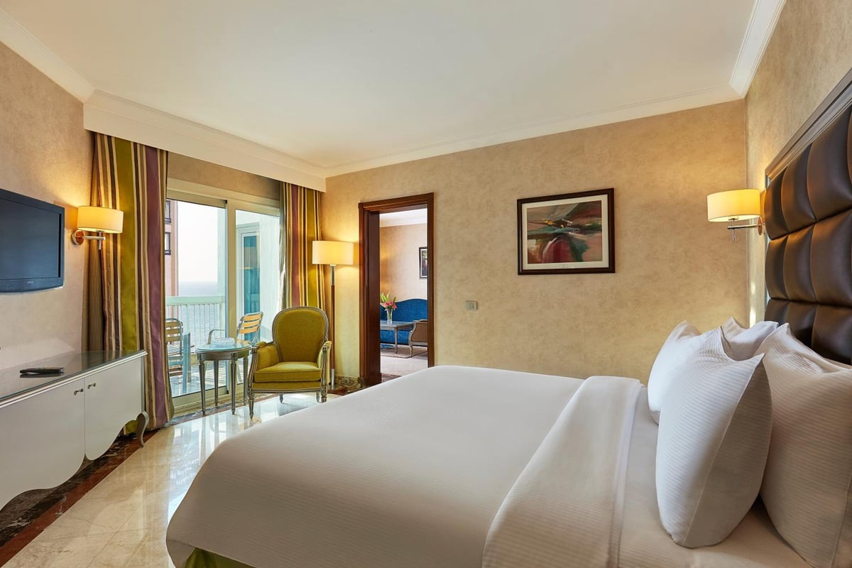 Hilton Alexandria Corniche bedroom with a large bed and balcony doors.