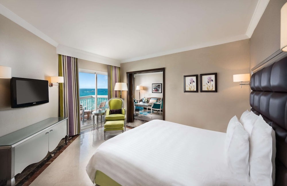 Hilton Alexandria Corniche bedroom with a sea-view balcony and adjoining sitting area.