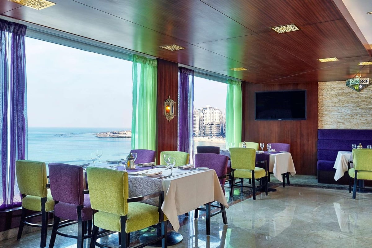 Hilton Alexandria Corniche restaurant dining room with large windows and a sea view.