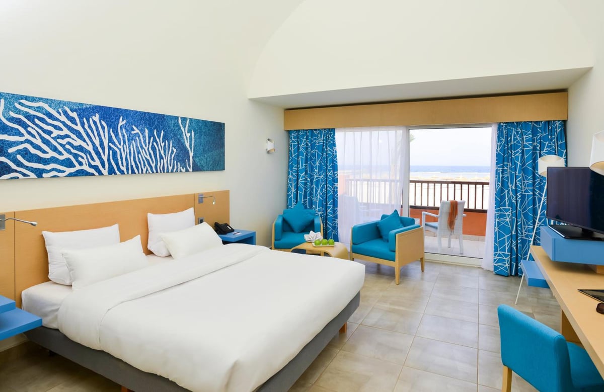 Novotel Marsa Alam Beach Resort guest room with a white bed and blue seating area.