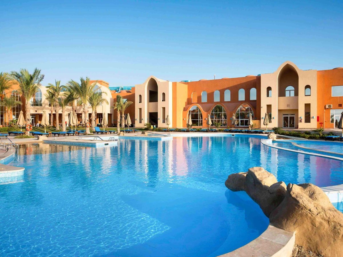 Novotel Marsa Alam Beach Resort pool area with a rock feature and arched buildings.