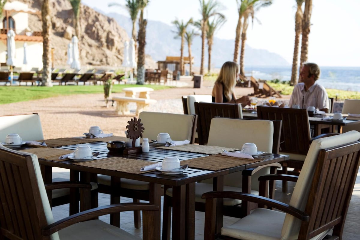 Dahab Paradise outdoor dining terrace with set dining tables and palm trees.