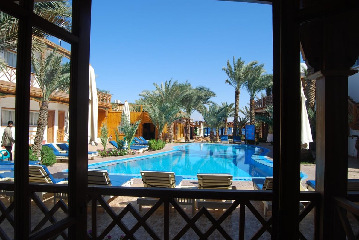 Acacia Dahab Hotel pool courtyard with a blue pool and palm trees.