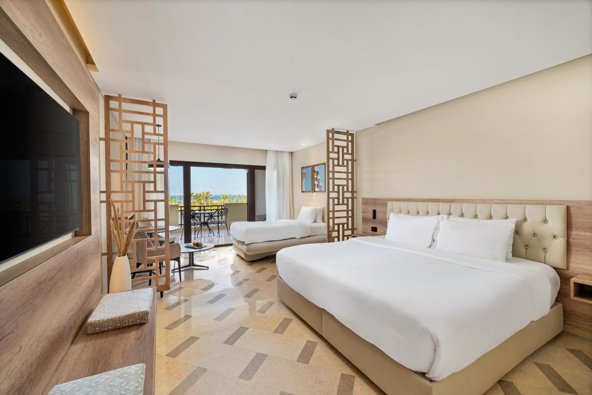 Steigenberger Aldau Beach Hotel bedroom with two beds and glass balcony doors.