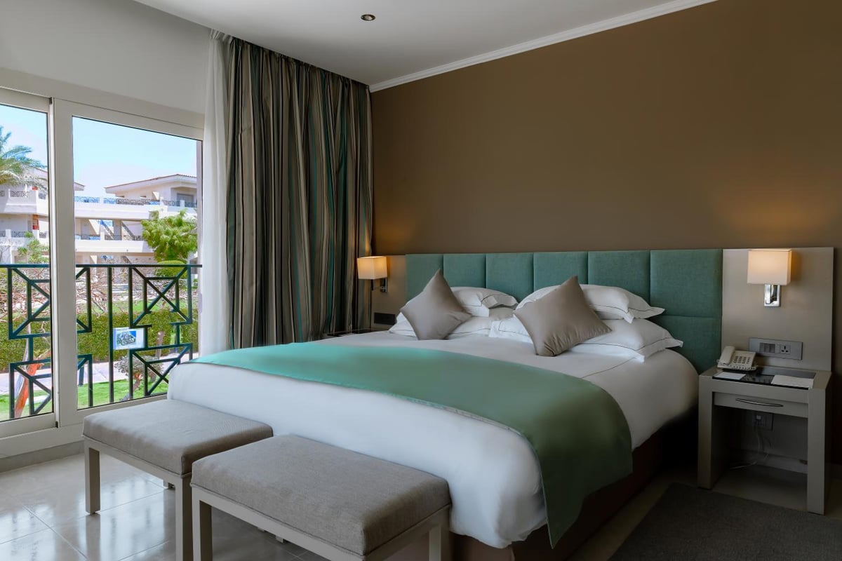 Cleopatra Luxury Resort Makadi Bay guest bedroom with a teal headboard and balcony doors.