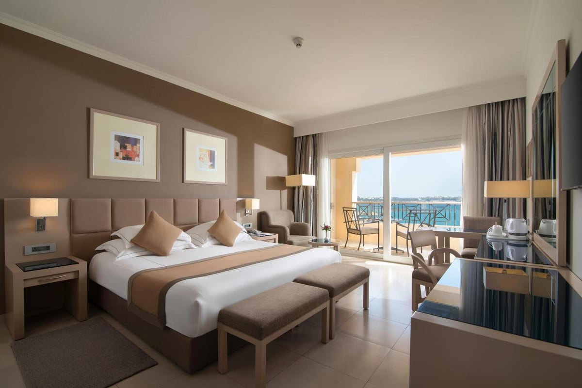Cleopatra Luxury Resort Makadi Bay bedroom with an upholstered bed and a balcony overlooking water.
