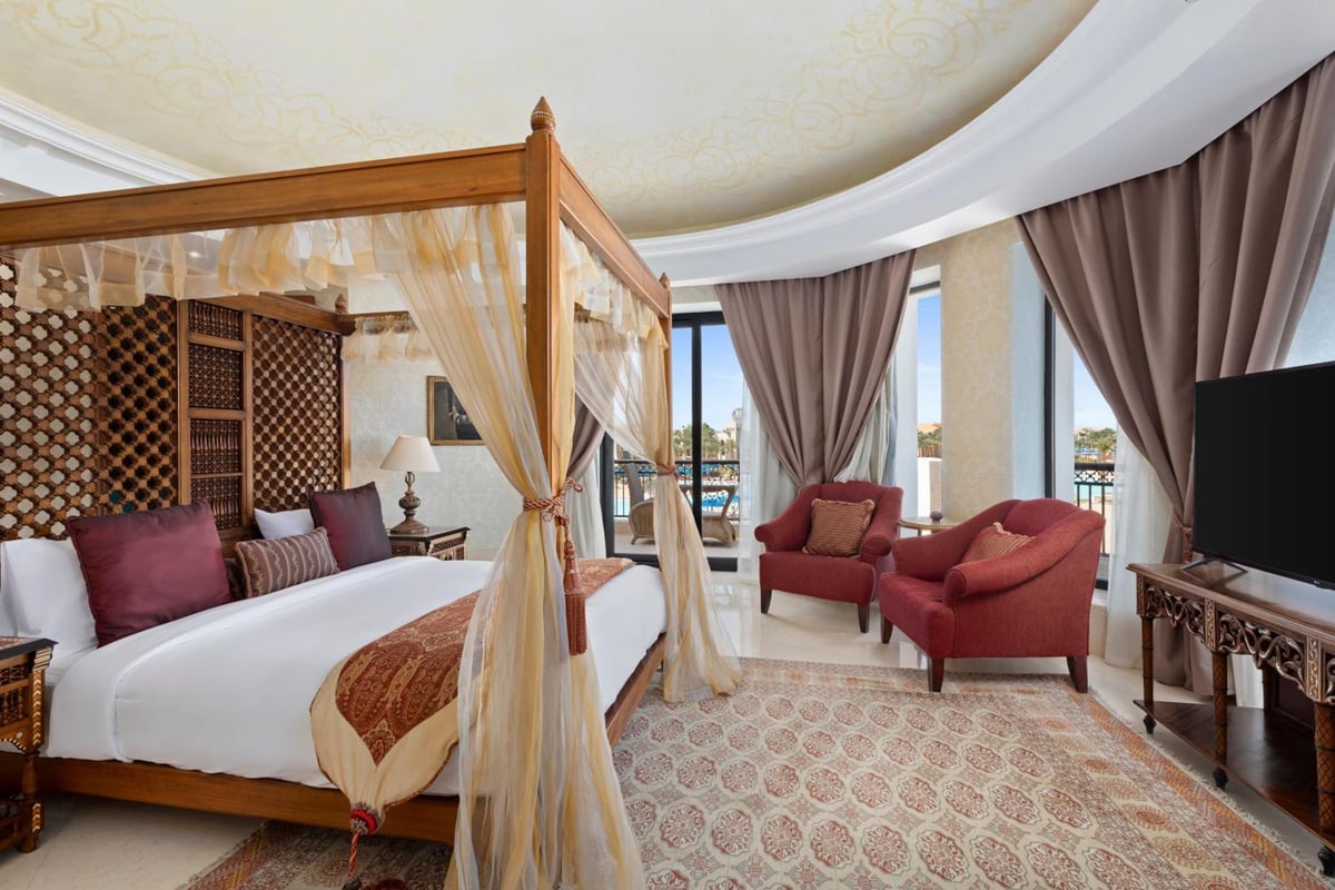 Pickalbatros The Palace Port Ghalib bedroom with a four-poster bed and red armchairs.