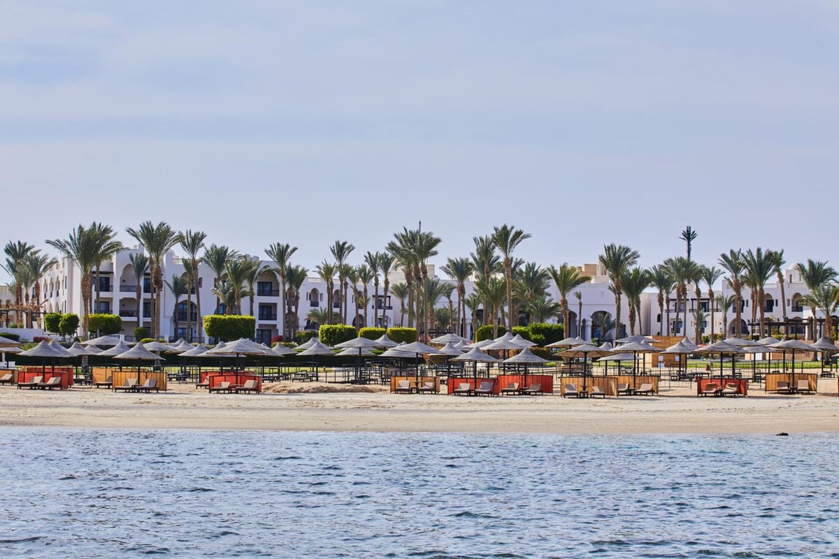 Pickalbatros The Palace Port Ghalib beach with palm trees and umbrellas.