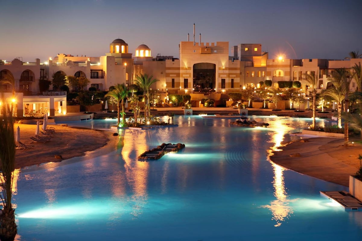 Pickalbatros The Palace Port Ghalib resort pool with blue-lit water and illuminated buildings.