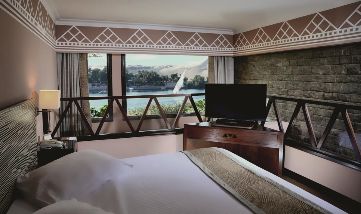 Movenpick Resort Aswan bedroom with a large bed and a river view.
