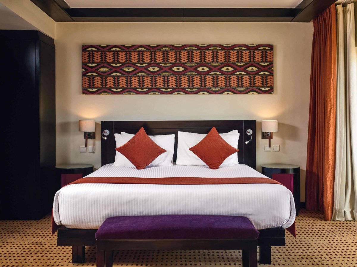 Movenpick Resort Aswan guest room with a king bed and a patterned wall hanging.