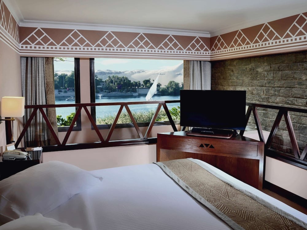 Movenpick Resort Aswan bedroom with a river view and a television.