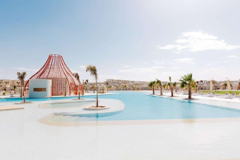 SENTIDO Reef Oasis Suakin Resort pool with turquoise water and a red metal structure.