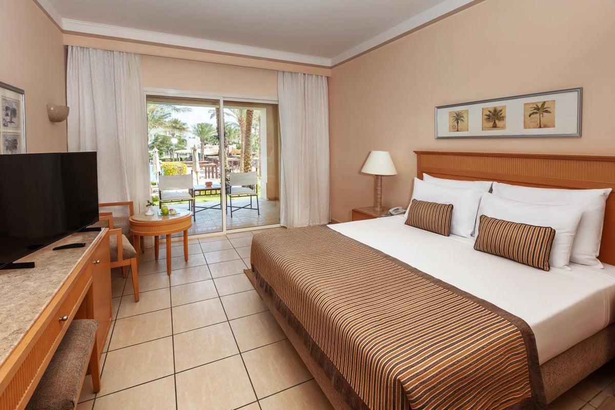 JAZ Makadi Star & Spa (Adults Only) bedroom with a patterned bedspread and sliding glass doors.