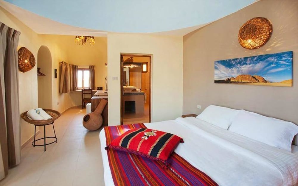 The Bedouin Moon Hotel Dahab bedroom with a white bed and a colorful striped throw.