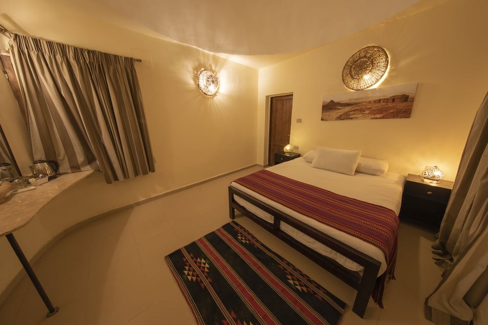The Bedouin Moon Hotel Dahab bedroom with a striped bedcover and wall sconces.