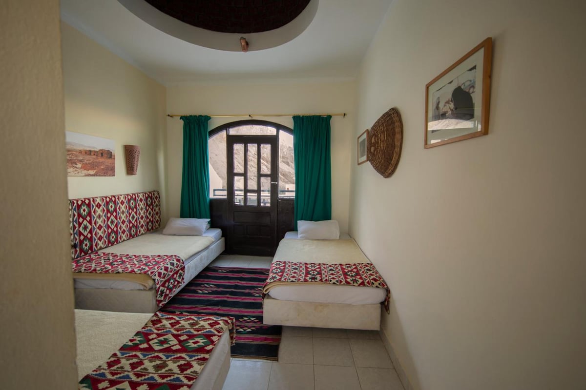 The Bedouin Moon Hotel Dahab twin bedroom with two patterned beds and an arched glass door.