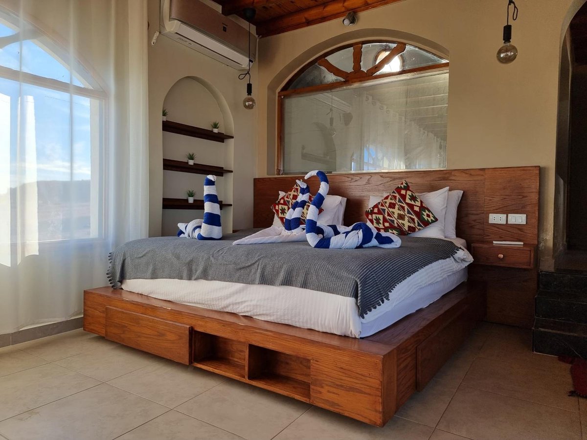 The Bedouin Moon Hotel Dahab bedroom with a wooden bed frame and arched window.