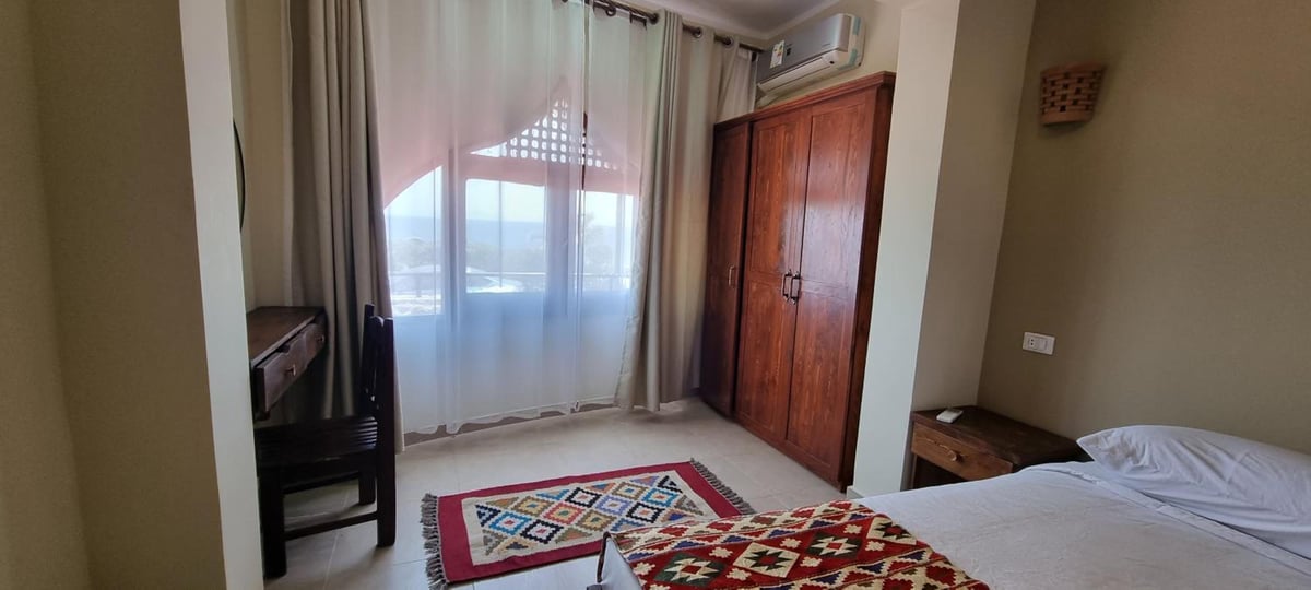 The Bedouin Moon Hotel Dahab bedroom with a wooden wardrobe and sheer-curtained window.