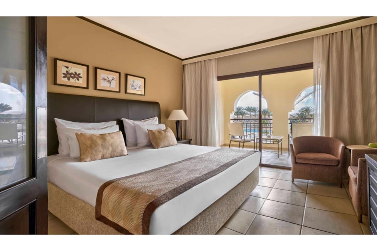 JAZ Lamaya Resort guest room with a large bed and sliding glass doors.