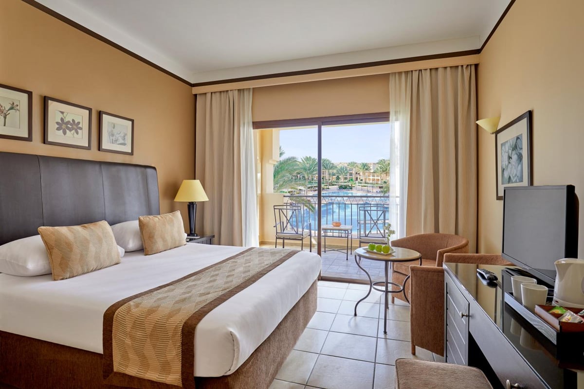 JAZ Lamaya Resort guest room with a king bed and a balcony overlooking the water.