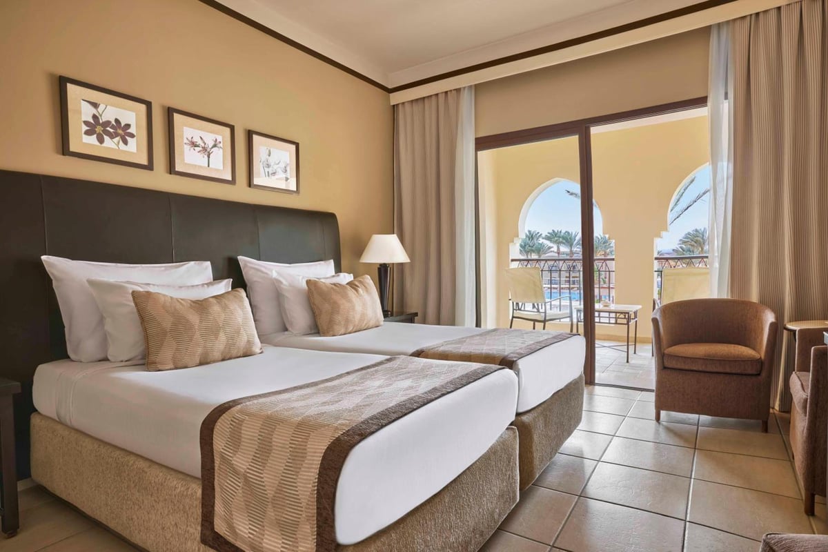 JAZ Lamaya Resort twin bedroom with two beds and arched balcony doors.