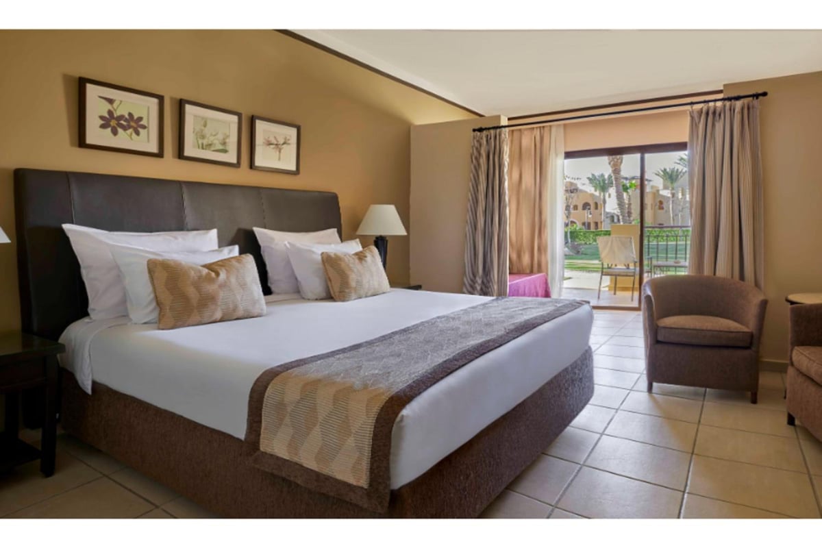 JAZ Lamaya Resort bedroom with an upholstered headboard and sliding glass doors.