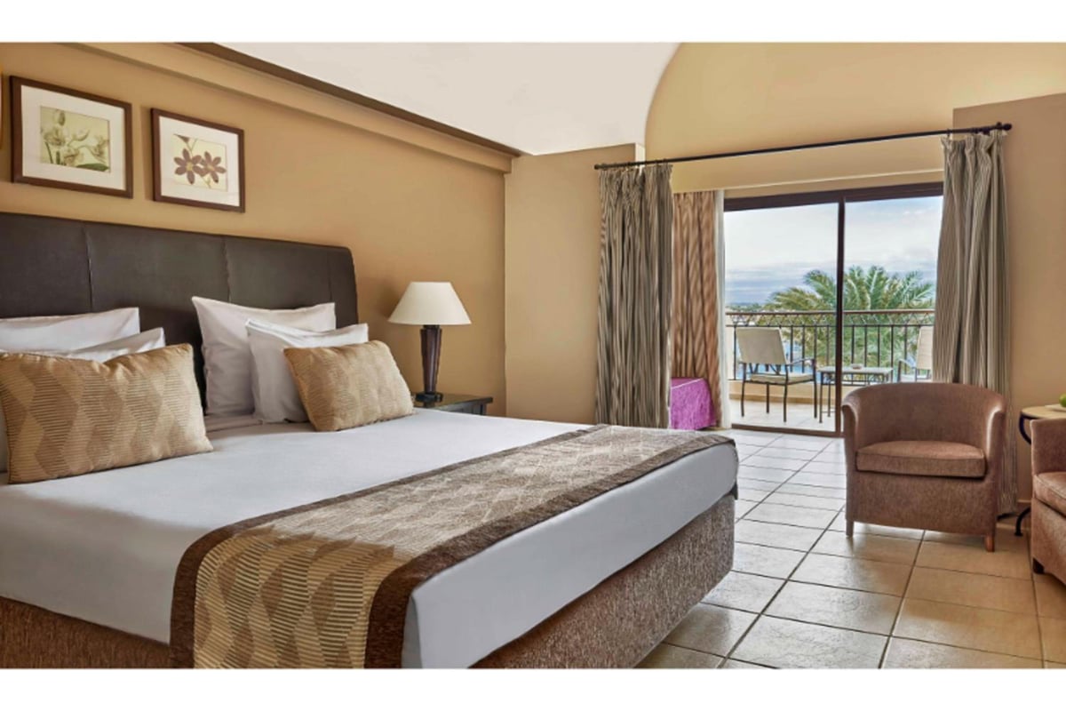 JAZ Lamaya Resort guest room with an upholstered headboard and balcony doors.