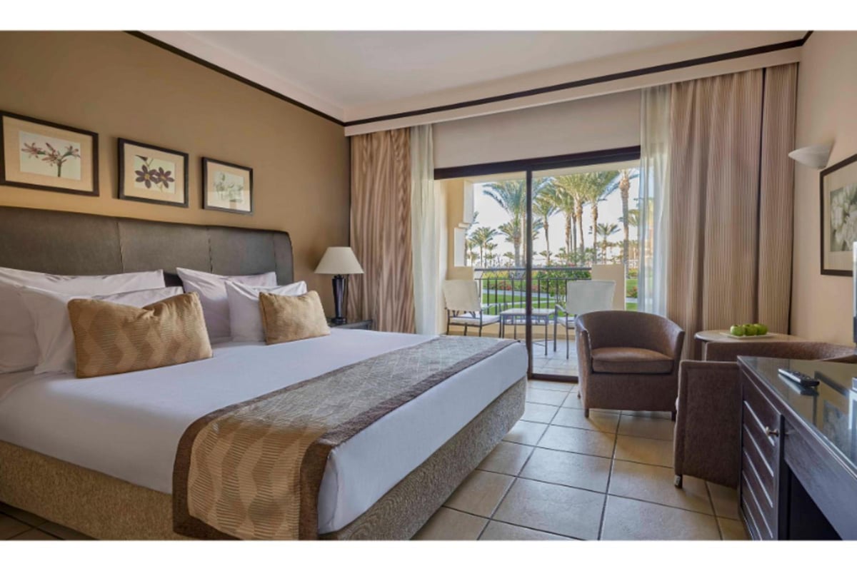 JAZ Lamaya Resort guest room with a large bed and sliding glass doors.