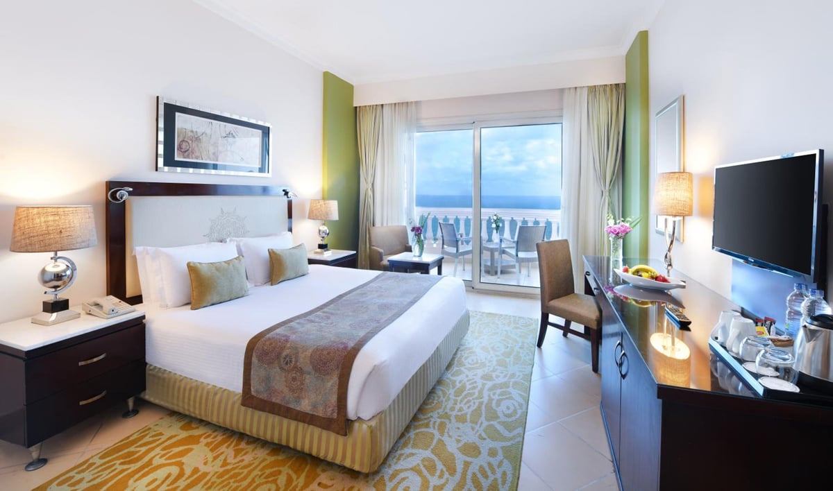 Tolip Hotel Alexandria bedroom with a large bed and a balcony overlooking the sea.
